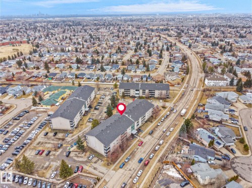 Aerial view showcasing the property's location within a developed neighborhood, featuring surrounding residential buildings, a road, and ample parking areas - 214 2620 Mill Woods Road E, Edmonton, AB - Outdoor With View