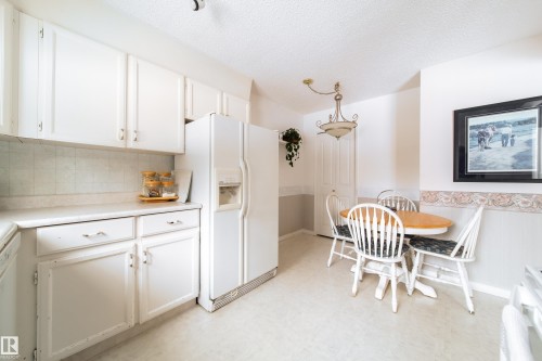 The property features a kitchen with white cabinetry, a side-by-side refrigerator, and a dedicated dining area with a chandelier - 11 Granada Place, St. Albert, AB - Indoor