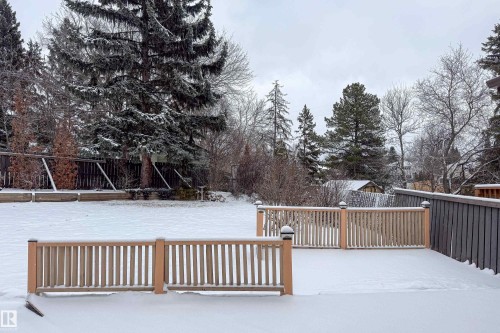 The property features a spacious deck with light-toned wooden railings, overlooking a snow-covered yard with mature evergreen trees and a wooden fence - 11 Granada Place, St. Albert, AB - Outdoor