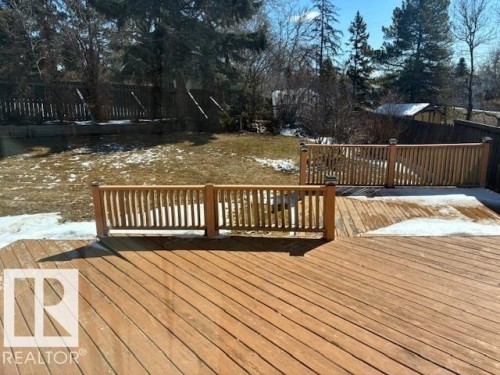 The property features an expansive wooden deck with railings, overlooking a yard with a partial lawn and mature trees - 11 Granada Place, St. Albert, AB - Outdoor With Deck Patio Veranda