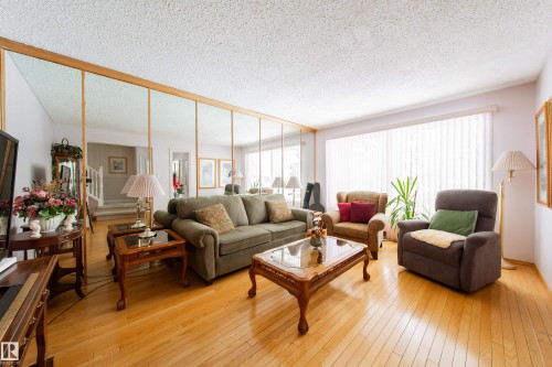 Living area featuring hardwood floors, a full wall of mirrors, and a large window with vertical blinds - 11 Granada Place, St. Albert, AB - Indoor Photo Showing Living Room
