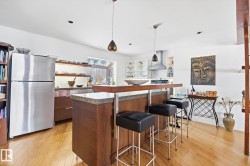Open-concept kitchen with hardwood floors, a breakfast bar, and stainless steel appliances, including a range hood and refrigerator - 