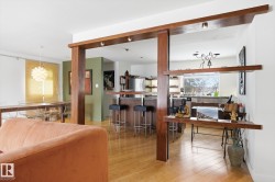 Living area featuring light wood flooring, a decorative wood partition with integrated shelving, and a view into the kitchen area - 