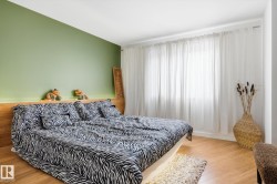 This bedroom features warm-toned wooden flooring, a light green accent wall, and a large window dressed with white sheer curtains - 