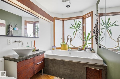 This bathroom features a contemporary vanity with a vessel sink and wall-mounted faucet, alongside a built-in corner bathtub - 11026 110 Avenue, Edmonton, AB - Indoor Photo Showing Bathroom