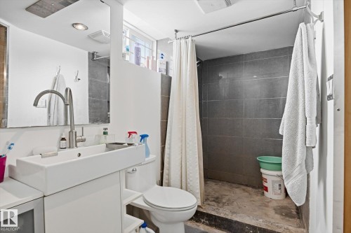 The bathroom features a modern rectangular vessel sink with a contemporary faucet, a toilet, and a tiled shower area with a shower curtain - 11026 110 Avenue, Edmonton, AB - Indoor Photo Showing Bathroom