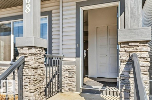 The property features a welcoming entrance with stone-clad pillars, black railings, and a light-colored siding facade - 3708 42 Avenue, Beaumont, AB - Outdoor