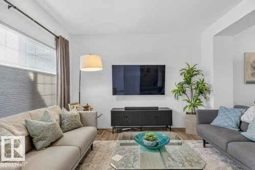 Inviting living area featuring light-colored walls, a large window with blinds and curtains, and hardwood flooring visible at the edges of the rug - 3708 42 Avenue, Beaumont, AB - Indoor Photo Showing Living Room