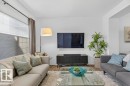 Inviting living area featuring light-colored walls, a large window with blinds and curtains, and hardwood flooring visible at the edges of the rug - 3708 42 Avenue, Beaumont, AB  - Indoor Photo Showing Living Room 