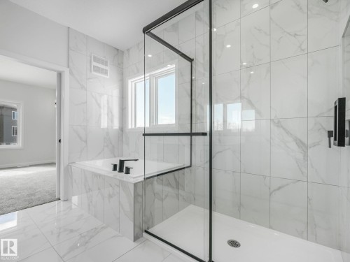 Spacious bathroom featuring large format marble-look tile flooring and walls, a built-in bathtub with matte black fixtures, and a glass-enclosed shower with matte black trim - 239 Kinglet Boulevard Nw, Edmonton, AB - Indoor Photo Showing Bathroom