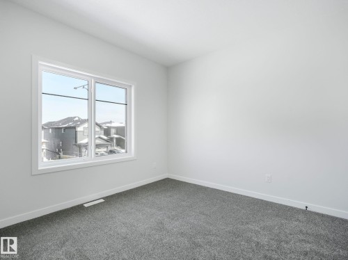 This room features light gray walls, dark gray carpet, and a large window with white trim - 239 Kinglet Boulevard Nw, Edmonton, AB - Indoor Photo Showing Other Room