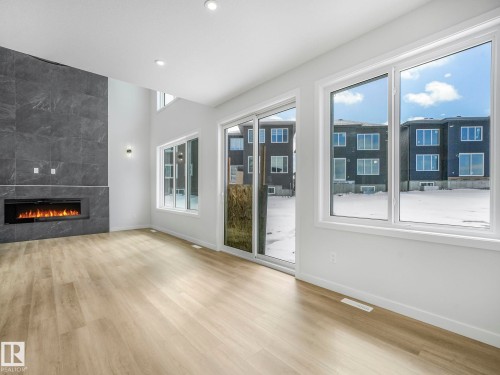 Living area featuring light wood-style flooring, a dark tiled accent wall with an inset fireplace, large windows, and a glass sliding door - 239 Kinglet Boulevard Nw, Edmonton, AB - Indoor With Fireplace