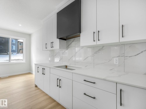 The property features a kitchen with white cabinetry, matte black hardware, a black range hood, and a white countertop with a matching backsplash - 239 Kinglet Boulevard Nw, Edmonton, AB - Indoor Photo Showing Kitchen