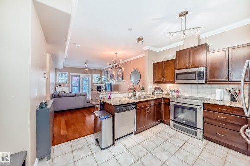 The kitchen features dark wood cabinetry, stainless steel appliances, and a tiled floor, with a view into a living area with hardwood floors - 307 10121 80 Avenue, Edmonton, AB - Indoor Photo Showing Kitchen With Stainless Steel Kitchen