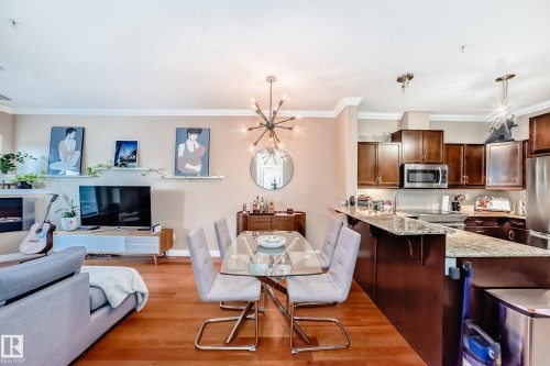 The open concept living area features hardwood floors, crown molding, and a modern light fixture above the dining space - 307 10121 80 Avenue, Edmonton, AB - Indoor Photo Showing Kitchen With Stainless Steel Kitchen