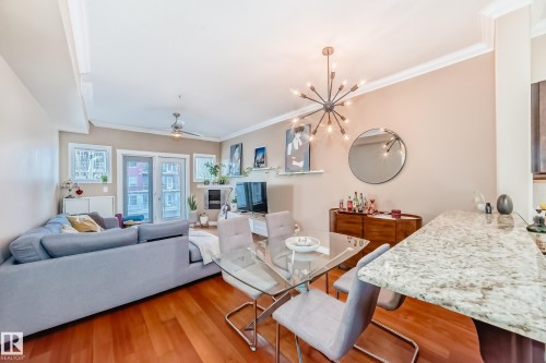 Open concept living space featuring hardwood floors, crown molding, a modern chandelier, and a granite breakfast bar - 307 10121 80 Avenue, Edmonton, AB - Indoor