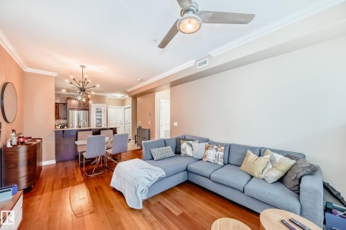 The open-concept living space features warm-toned hardwood flooring, crown molding, and a ceiling fan with integrated lighting - 307 10121 80 Avenue, Edmonton, AB - Indoor Photo Showing Living Room