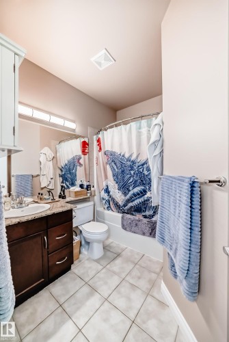 This bathroom features a vanity with dark wood cabinetry and a light-colored countertop, a toilet, and a bathtub with a shower curtain - 307 10121 80 Avenue, Edmonton, AB - Indoor Photo Showing Bathroom