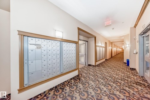 The property features a well-maintained hallway with a patterned carpet, wall-mounted light fixtures, and individual mailboxes for residents - 307 10121 80 Avenue, Edmonton, AB - Indoor Photo Showing Other Room