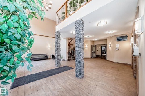 An inviting entryway featuring wood-look tile flooring, stacked stone pillars, and a visible second-level railing - 307 10121 80 Avenue, Edmonton, AB - Indoor Photo Showing Other Room