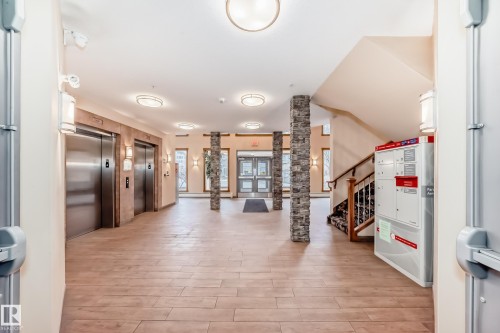 The property features a spacious lobby with wood-look tile flooring, two elevators with brushed metal doors, and a stone-clad pillar - 307 10121 80 Avenue, Edmonton, AB - Indoor Photo Showing Other Room