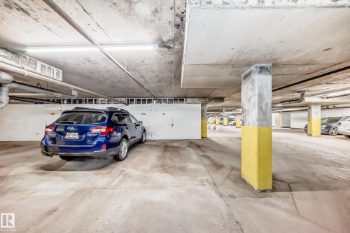 Underground parking garage featuring concrete flooring and ceilings, with storage units lining one wall - 307 10121 80 Avenue, Edmonton, AB - Indoor Photo Showing Garage