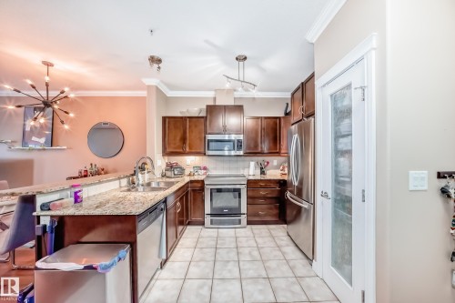 Well-appointed kitchen featuring granite countertops, stainless steel appliances, dark wood cabinetry, and tiled flooring - 307 10121 80 Avenue, Edmonton, AB - Indoor Photo Showing Kitchen With Stainless Steel Kitchen With Double Sink