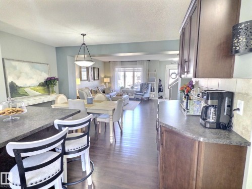 The open concept living area features dark hardwood flooring, light blue and grey painted walls, and a recessed ceiling with a modern light fixture - 5718 Rue Eaglemont, Beaumont, AB - Indoor