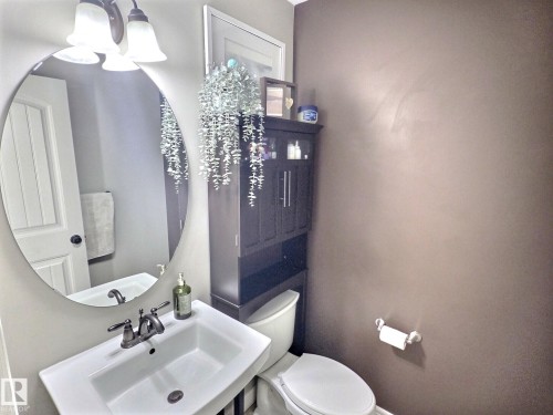 Bathroom featuring a white pedestal sink with a dual-handle faucet, an oval wall-mounted mirror, and a dark wood storage cabinet - 5718 Rue Eaglemont, Beaumont, AB - Indoor Photo Showing Bathroom
