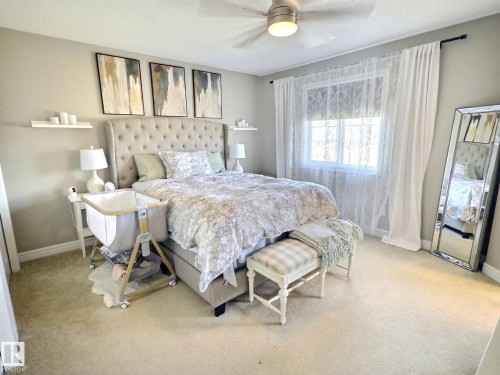 This bedroom features a generously sized bed with a tufted headboard, carpeted flooring, and a window providing natural light - 5718 Rue Eaglemont, Beaumont, AB - Indoor Photo Showing Bedroom