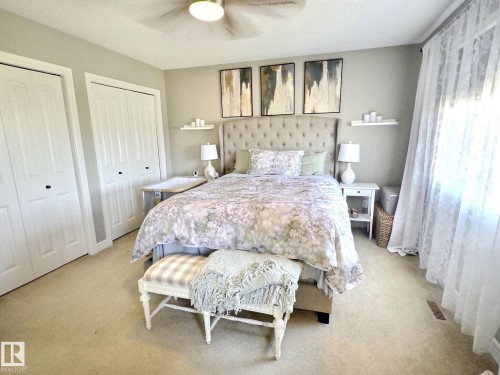This bedroom features light-colored carpeting, a ceiling fan, and two white bi-fold closet doors - 5718 Rue Eaglemont, Beaumont, AB - Indoor Photo Showing Bedroom