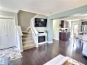 This inviting living space features dark hardwood flooring, a fireplace, and a carpeted staircase with white railings - 5718 Rue Eaglemont, Beaumont, AB  - Indoor Photo Showing Living Room With Fireplace 