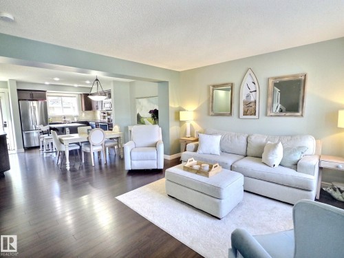 Open concept living area with dark hardwood floors, recessed lighting, and a kitchen featuring stainless steel appliances and dark cabinetry - 5718 Rue Eaglemont, Beaumont, AB - Indoor Photo Showing Living Room