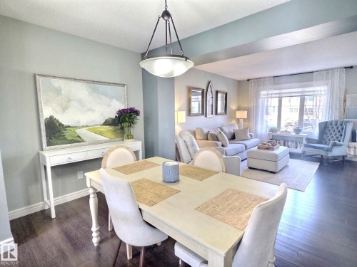 Spacious open-concept living area featuring dark wood flooring, a dining area with a chandelier, and a living room with a large window - 5718 Rue Eaglemont, Beaumont, AB - Indoor