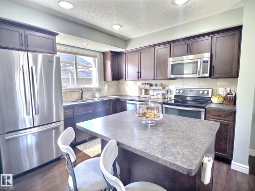 The kitchen features a center island with a countertop, dark wood cabinetry, stainless steel appliances, and recessed lighting - 5718 Rue Eaglemont, Beaumont, AB - Indoor Photo Showing Kitchen With Stainless Steel Kitchen With Double Sink
