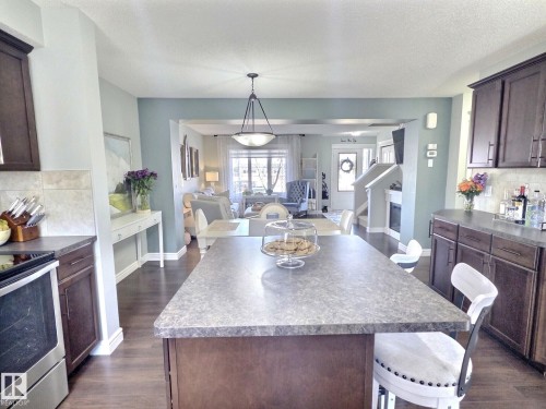 The property features an open-concept layout with a kitchen island, dark wood cabinetry, and stainless steel appliances - 5718 Rue Eaglemont, Beaumont, AB - Indoor Photo Showing Kitchen With Upgraded Kitchen