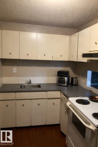 The kitchen features a white electric range, a stainless steel sink, and white cabinetry with gray countertops - 4 3819 76 Street, Edmonton, AB - Indoor Photo Showing Kitchen