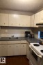 The kitchen features a white electric range, a stainless steel sink, and white cabinetry with gray countertops - 4 3819 76 Street, Edmonton, AB  - Indoor Photo Showing Kitchen 