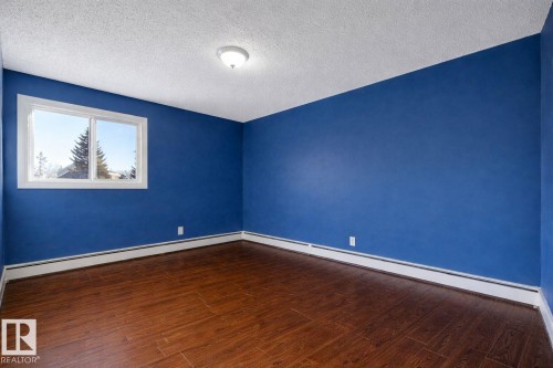 This room features rich wood flooring, bright blue walls, and a window providing natural light and a view of trees - 4 3819 76 Street, Edmonton, AB - Indoor Photo Showing Other Room