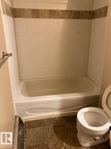 Bathroom featuring a bathtub, tiled shower walls with a decorative accent band, and a toilet - 4 3819 76 Street, Edmonton, AB - Indoor Photo Showing Bathroom