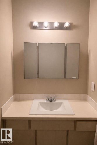 Bathroom vanity featuring a light-colored countertop, an integrated sink, and a tri-fold medicine cabinet, illuminated by a four-bulb light fixture - 4 3819 76 Street, Edmonton, AB - Indoor Photo Showing Bathroom