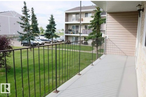 The property features a private balcony with a metal railing, overlooking a green lawn area and mature evergreen trees - 4 3819 76 Street, Edmonton, AB - Outdoor With Balcony With Exterior