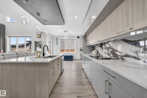 The kitchen showcases light-toned cabinetry, a spacious island with a sink, and an elegant patterned backsplash - 449 Roberts Crescent, Leduc, AB - Indoor Photo Showing Kitchen With Double Sink With Upgraded Kitchen