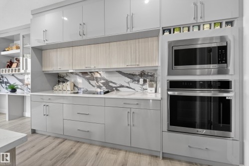 The kitchen features light wood flooring, light grey cabinetry, a light-colored countertop, and a white marble backsplash with grey veining - 449 Roberts Crescent, Leduc, AB - Indoor Photo Showing Kitchen