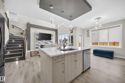 The property features an open-concept living area with light wood-style flooring and a staircase with carpeted treads and integrated lighting - 449 Roberts Crescent, Leduc, AB - Indoor Photo Showing Kitchen With Double Sink