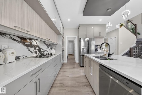 The kitchen features a spacious island with a sink and a black faucet, light wood cabinetry, white countertops, and a striking marble backsplash - 449 Roberts Crescent, Leduc, AB - Indoor Photo Showing Kitchen With Double Sink With Upgraded Kitchen