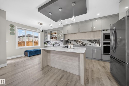 The kitchen features a central island with a white countertop, light wood flooring, gray cabinetry, and a stainless steel refrigerator - 449 Roberts Crescent, Leduc, AB - Indoor Photo Showing Kitchen With Upgraded Kitchen