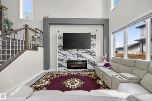 Living area featuring high ceilings, a fireplace with a marble-style surround, and large windows providing ample natural light - 449 Roberts Crescent, Leduc, AB - Indoor Photo Showing Living Room With Fireplace
