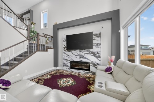 This living area features a modern fireplace with a marble-style surround, a staircase with contemporary railings, and large windows providing natural light - 449 Roberts Crescent, Leduc, AB - Indoor Photo Showing Living Room With Fireplace