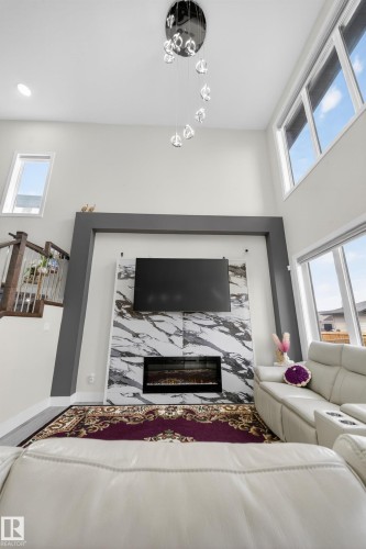 The living area features a high ceiling with a contemporary chandelier, a fireplace with a striking marble-patterned surround, and tall windows that provide abundant natural light - 449 Roberts Crescent, Leduc, AB - Indoor